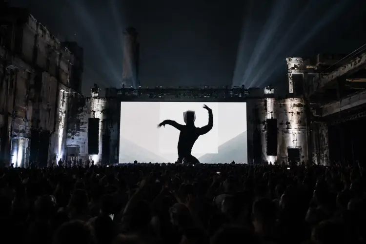 Silhouetted dancer on a massive festival screen, crowd with hands raised
