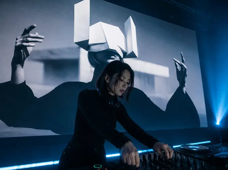 DJ performing with an OOVIE cinematic figure on the big screen behind the booth